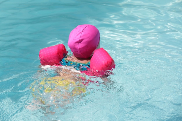 Bambino in piscina con galleggiante rosa con acqua blu