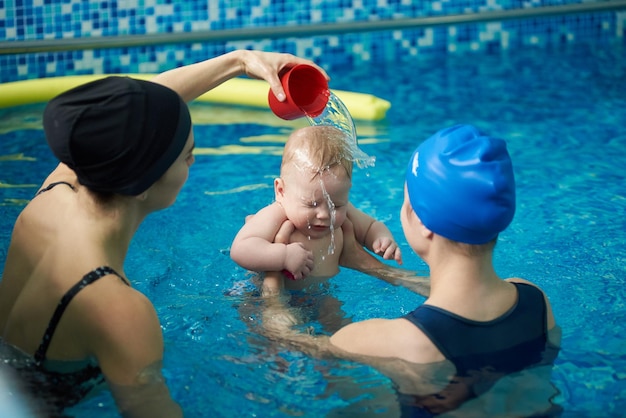 Bambino in piscina e due donne Ragazzino spaventato e tenendo gli occhi chiusi mentre la donna versava acqua sulla sua testa