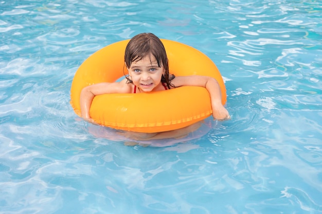 Bambino in piscina sull'anello gonfiabile arancione Ragazza che impara a nuotare con l'anello interno arancione Gioco acquatico per neonati e bambini Attività sportiva sana all'aperto per bambini Divertimento in spiaggia per bambini