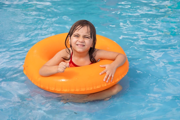 Bambino in piscina sull'anello gonfiabile arancione Ragazza che impara a nuotare con l'anello interno arancione Gioco acquatico per neonati e bambini Attività sportiva sana all'aperto per bambini Divertimento in spiaggia per bambini