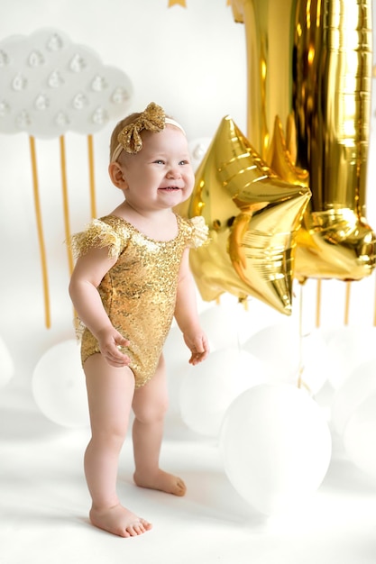 Bambino in tuta d'oro al primo compleanno su sfondo decorato con palloncini