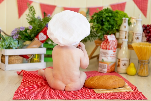 Bambino in un cappello da cuoco con cibo intorno a lui