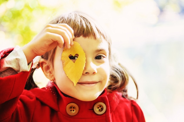 Bambino in un cappotto rosso con foglie d&#39;autunno. Amare l&#39;autunno Messa a fuoco selettiva