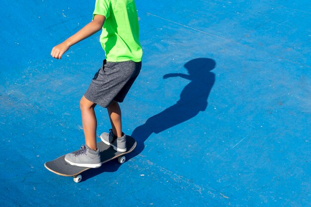 Bambino in un parco per skateboarder in una giornata di sole dove l'ombra piena si riflette sul terreno