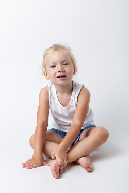 Bambino in una maglietta, pantaloncini seduti in studio su uno sfondo chiaro.