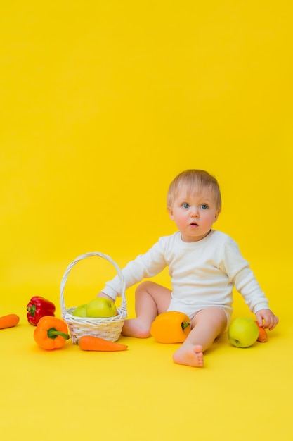 Bambino in una tuta bianca con verdure, seduto su uno sfondo giallo. cibo sano per il bambino, spazio per il testo