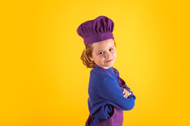 Bambino in uniforme da cucina e cappello da chef che prepara il cibo su sfondo a colori da studio Cucinare il concetto di cucina e cibo per bambini