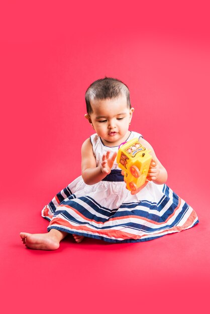 Bambino indiano o asiatico o neonato o bambino che gioca con giocattoli o blocchi mentre è sdraiato o seduto isolato su uno sfondo luminoso o colorato