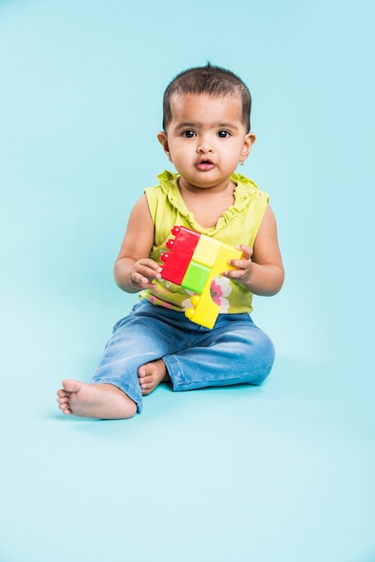 Bambino indiano o asiatico o neonato o bambino che gioca con giocattoli o blocchi mentre è sdraiato o seduto isolato su uno sfondo luminoso o colorato