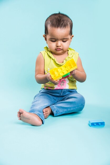 Bambino indiano o asiatico o neonato o bambino che gioca con giocattoli o blocchi mentre è sdraiato o seduto isolato su uno sfondo luminoso o colorato