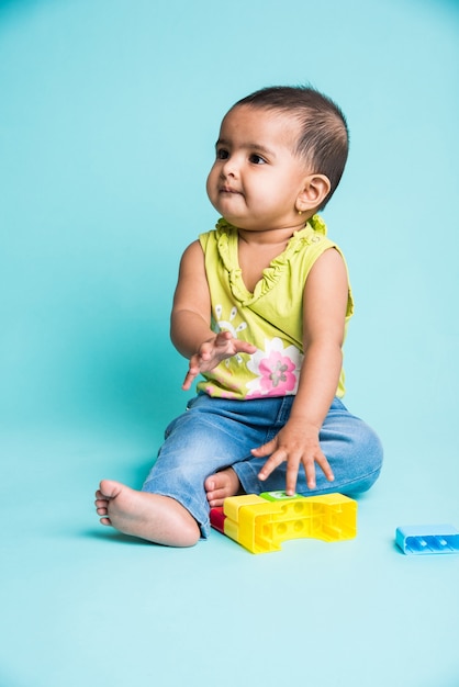 Bambino indiano o asiatico o neonato o bambino che gioca con giocattoli o blocchi mentre è sdraiato o seduto isolato su uno sfondo luminoso o colorato