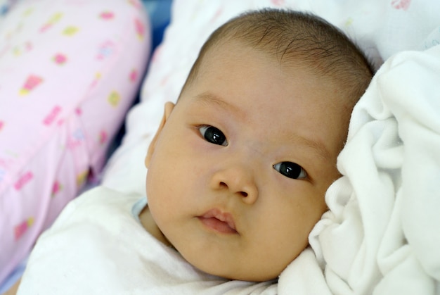 Bambino infantile asiatico sveglio in bello vestito che si trova e che guarda qualcosa sul suo letto.