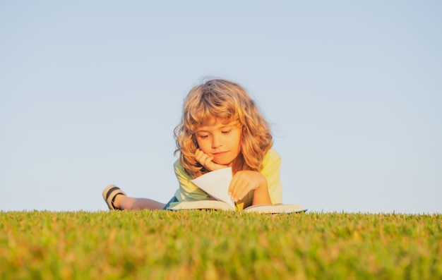 Bambino intelligente che legge un libro sdraiato sull'erba in campo sul cielo e sul campo in erba ritratto di bambini intelligenti