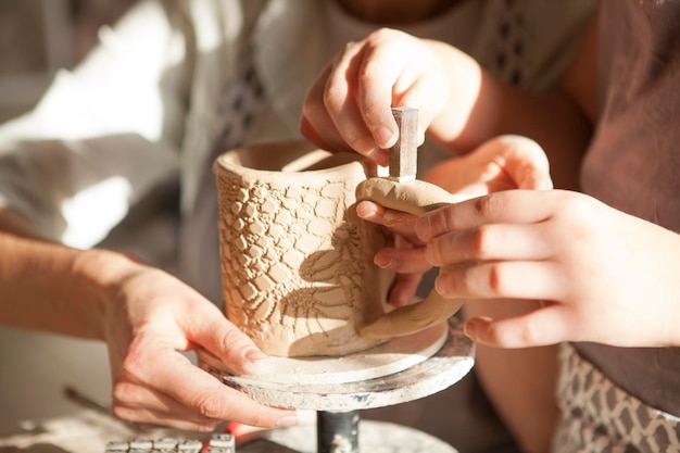 Bambino irriconoscibile che decora la ceramica con francobolli che aiutano la madre a lezione di ceramica