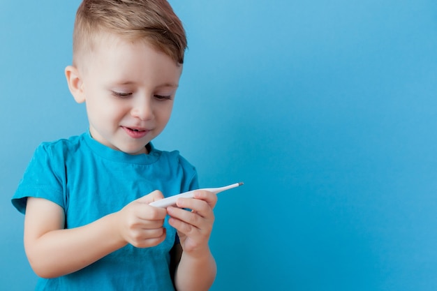 Bambino malato con un termometro, misurando l'altezza della sua febbre ed esaminando la fotocamera.