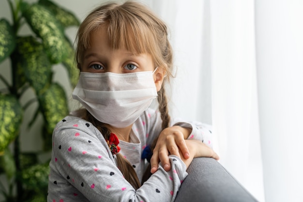 Bambino mascherato - protezione contro il virus dell'influenza. Piccola ragazza caucasica che indossa una maschera per proteggere pm2.5. Armi biologiche. bambino su uno sfondo grigio con spazio di copia. epidemico pandemico.