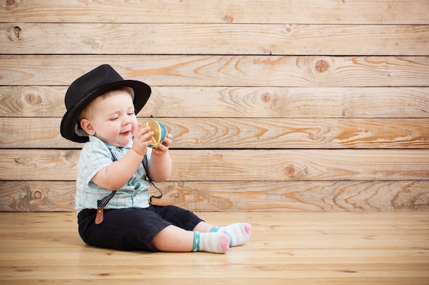 Bambino negli shorts black hat, della camicia e delle bretelle su fondo di legno