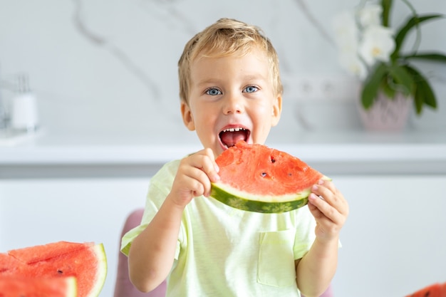 bambino nella cucina di casa un bambino mangia un'anguria sorride il concetto di un'alimentazione sana