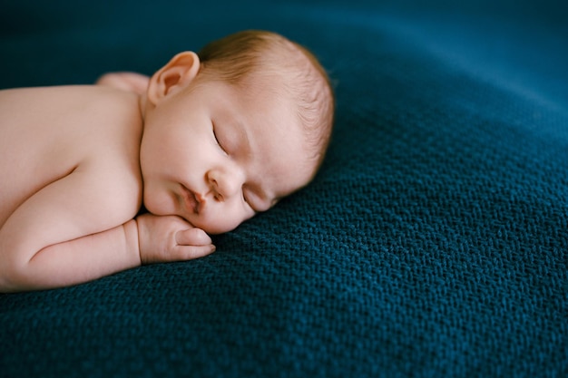 Bambino nudo che dorme su una coperta blu con la mano sotto la guancia