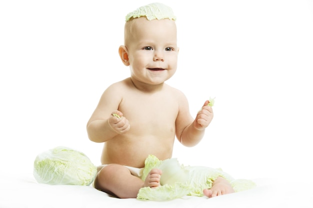 Bambino nudo in pannolino sta giocando con frutta e verdura biologica fresca isolati su uno sfondo bianco Ragazzino che morde una testa verde fresca di cavolo Cibo sano per il concetto di bambini