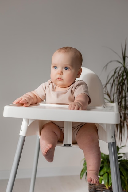 bambino paffuto in un body bianco si siede su un seggiolone bianco per l'alimentazione