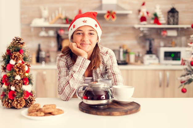 Bambino pensieroso che si gode il Natale e gustosi biscotti sul tavolo della cucina e sull'albero di Natale christmas