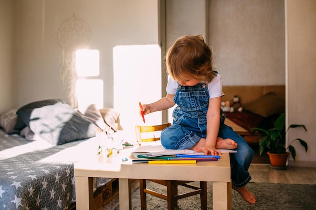 Bambino piccolo a casa al tavolo dei bambini disegna con pennarelli