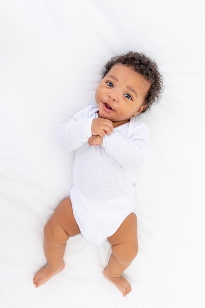 Bambino piccolo afroamericano su un letto bianco in camera da letto.