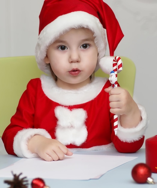 Bambino piccolo vestito da Babbo Natale che scrive una lettera con gli auguri per il nuovo anno