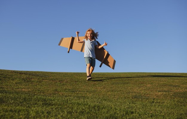 Bambino ragazzo che salta e corre con le ali di un aeroplano giocattolo Sogna di diventare un pilota Supereroe che vola