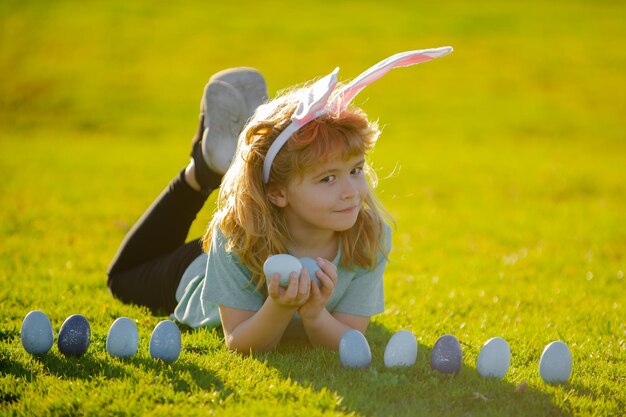 Bambino ragazzo con uova di Pasqua e orecchie da coniglio sull'erba bambino carino divertirsi nel parco caccia all'uovo di Pasqua conce