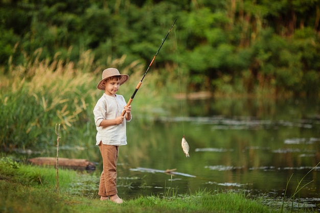 bambino ragazzo impegnato in hobby di pesca. si trova sulla riva del fiume in estate e tiene una canna da pesca con pesce pescato