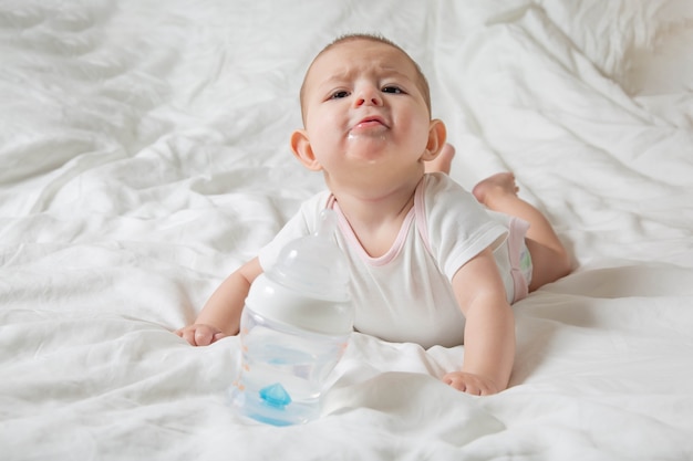 bambino sbavare e dentizione giacciono sul letto tirare le mani alla bottiglia d'acqua bambino giocherellona cupo