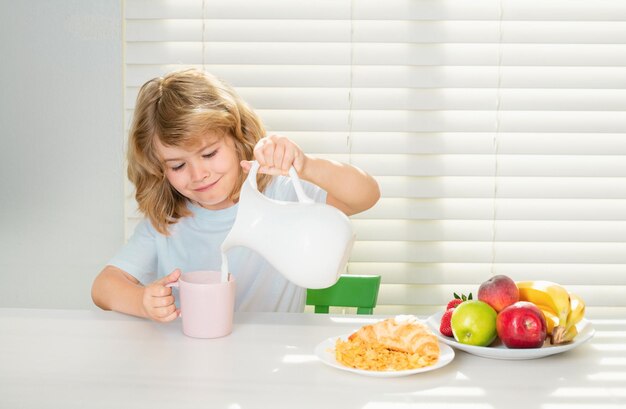 Bambino scolastico che versa latte di mucca intero per la colazione bambino in cucina al tavolo che mangia verdure