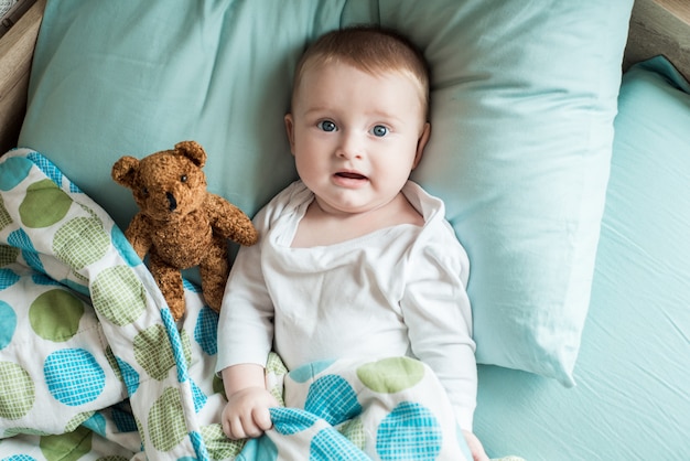 bambino sdraiato nel letto con un orsacchiotto di peluche