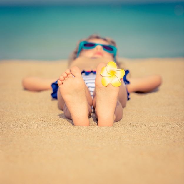 Bambino sdraiato su una spiaggia sabbiosa con un fiore giallo sul piede