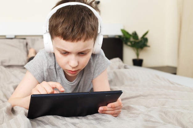 Bambino sdraiato sul letto a casa con tablet pc e lettura online