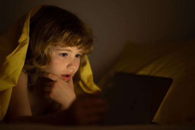 Bambino sdraiato sul letto e navigando in internet su tablet in camera oscura bambino utilizzando tablet pc di notte litt