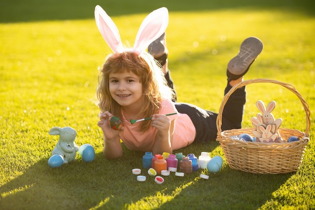 Bambino sdraiato sull'erba nel parco con le uova di pasqua coniglietto di pasqua bambini che dipingono le uova di pasqua bambino ragazzo in bu