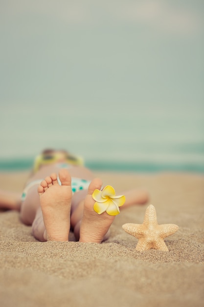 Bambino sdraiato sulla sabbia in spiaggia con un fiore sul piede e una stella marina sulla sabbia