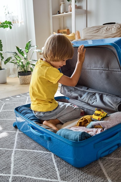 Bambino seduto in una valigia e giocando con un giocattolo in attesa di un viaggio in vacanza