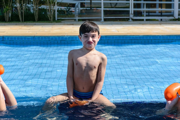Bambino seduto sul bordo della piscina e facendo una faccia buffa alla telecamera.