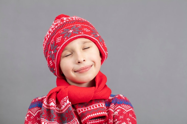 Bambino sognante in abiti caldi su uno sfondo grigio