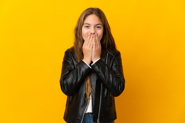 Bambino sopra la parete gialla isolata felice e sorridente che copre la bocca con le mani