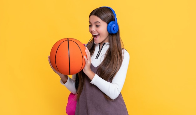 Bambino sorpreso in cuffia con zaino scolastico e palla da basket su sfondo giallo