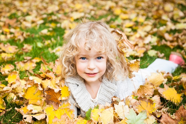 Bambino sorridente felice che si trova sulle foglie di acero gialle nel parco di autunno
