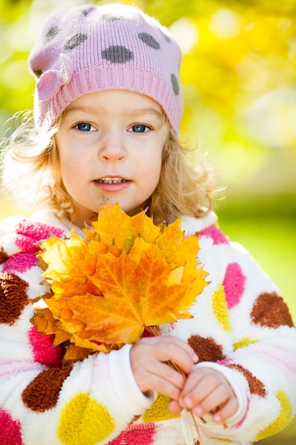 Bambino sorridente felice con le foglie di acero gialle nel parco di autunno