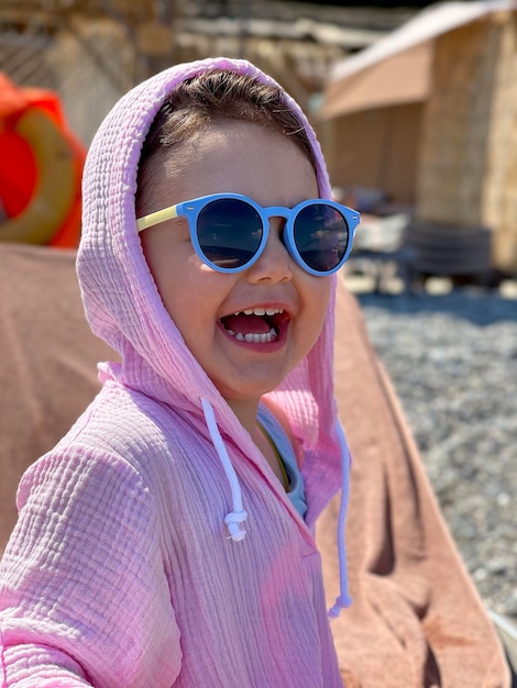 bambino sorridente felice in occhiali da sole e tunica rosa, bella bambina sulla spiaggia, foto sul telefono