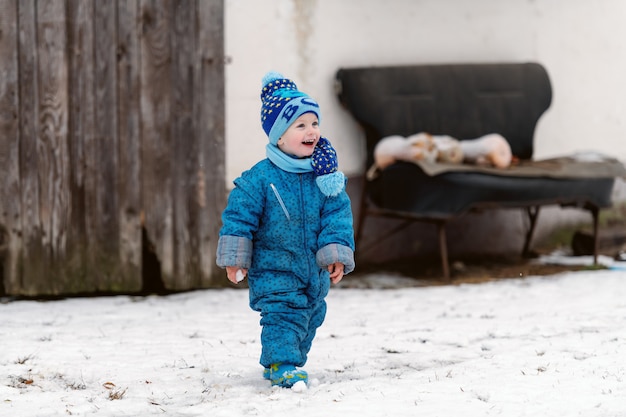 Bambino sorridente in abbigliamento invernale con cappello e sciarpa godendo sulla neve.