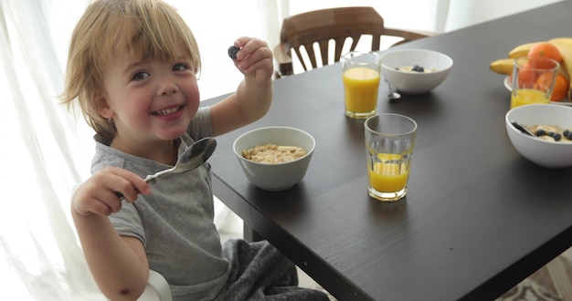 Bambino sta facendo colazione e guardando la fotocamera e sorridente al tavolo in camera